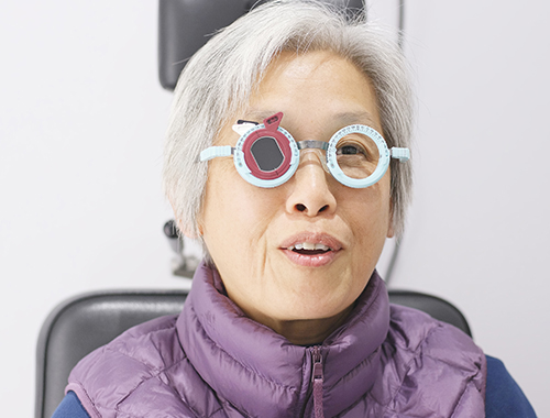 Image d'une femme âgée passant un test d'acuité visuelle avec un sourire aux lèvres.